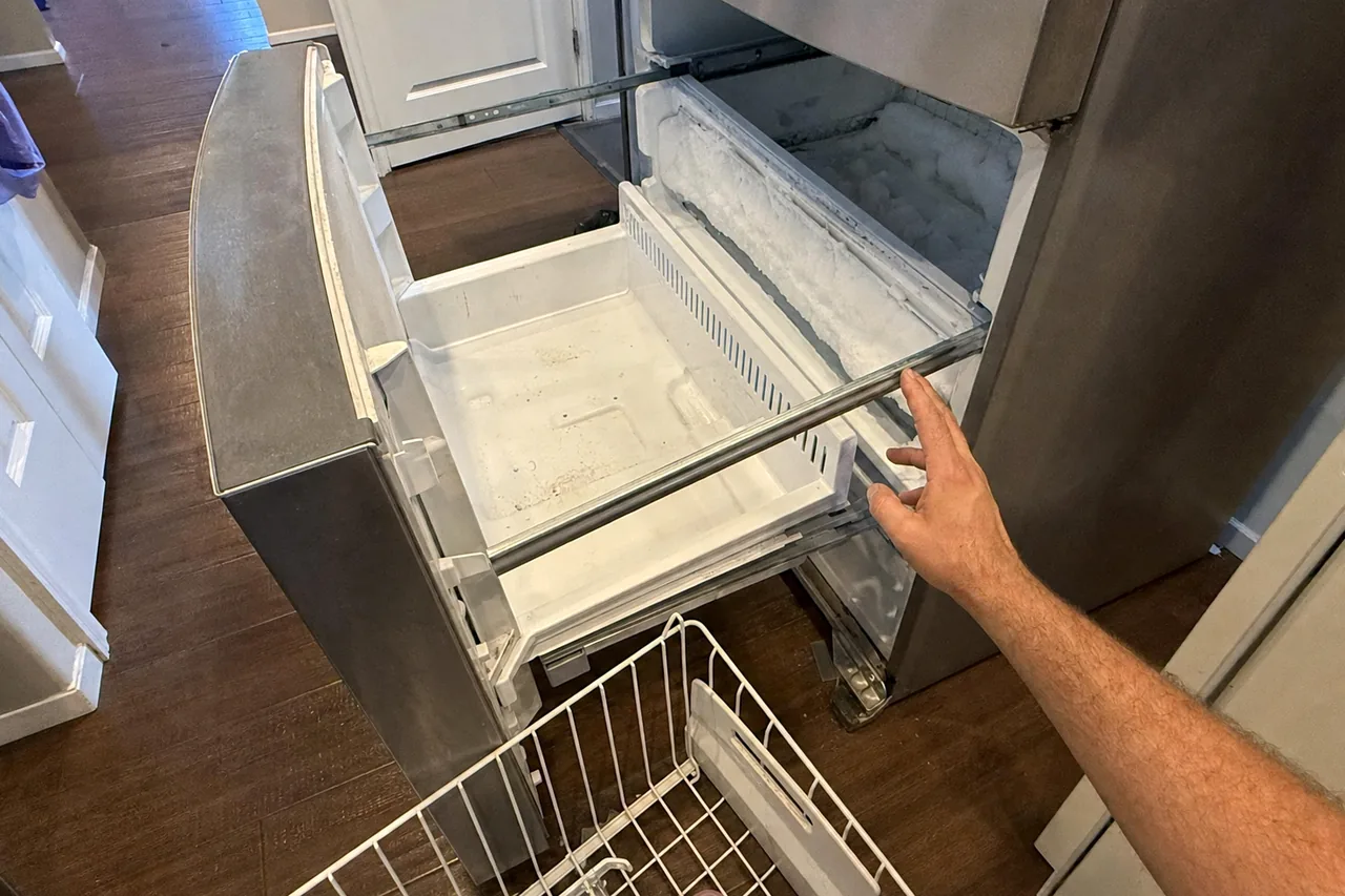A frosted freezer compartment seen over the top of an open drawer, the runner track exposed along the side.