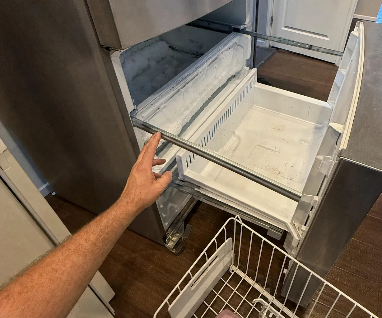 A drawer front pulled open at floor level, its runners extended and the empty basket standing beside it.