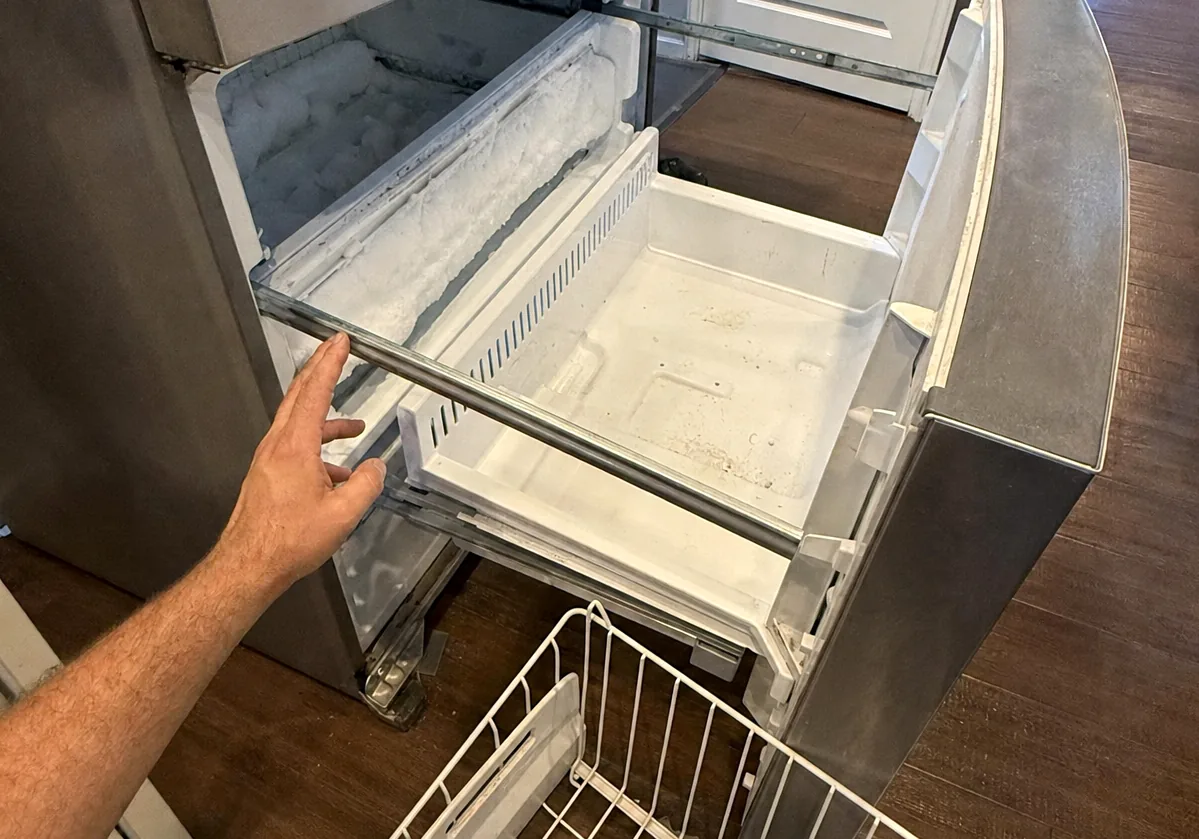 An open freezer drawer with its basket removed, the interior walls carrying an even layer of frost.