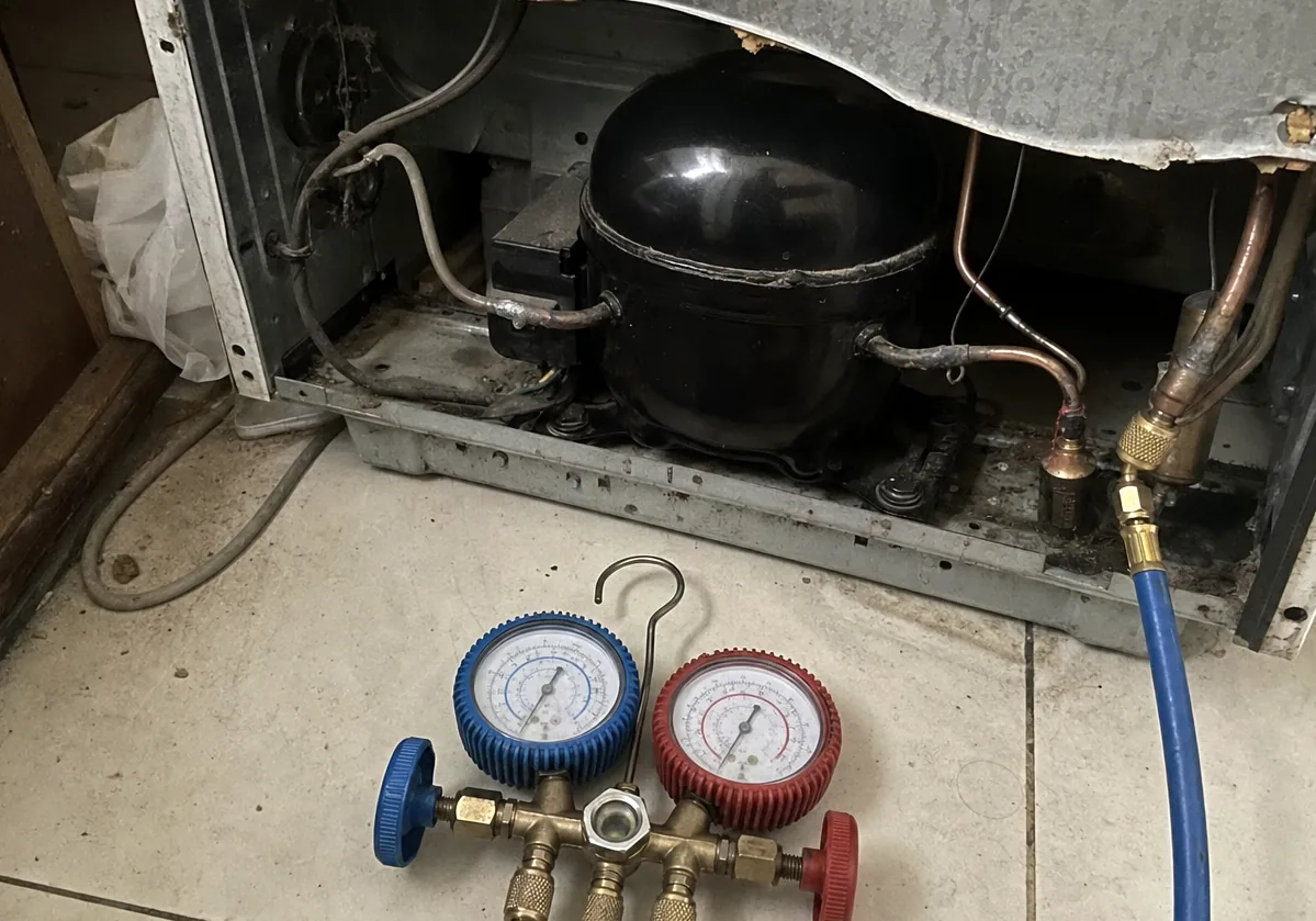Copper tubing and a black compressor dome in an open machine bay, manifold hoses laid across them.